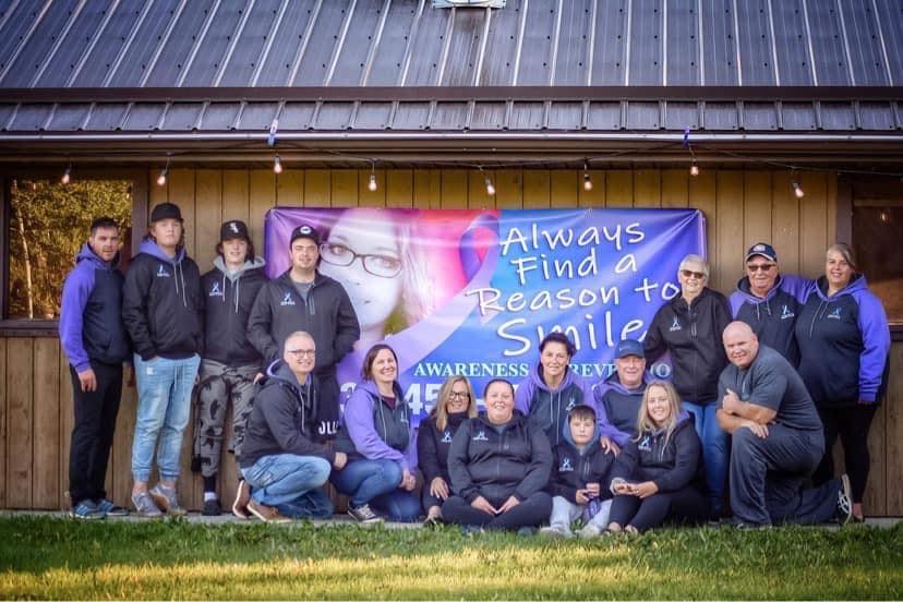 A large group in purple jackets standing in front of an Always Find a Reason to Smile banner