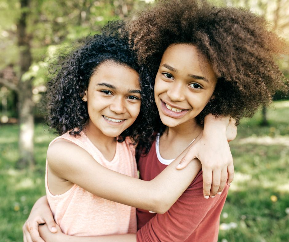 Two smiling girls hugging outdoors in a park