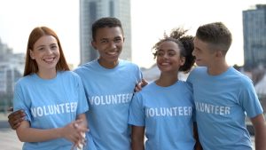 Four young volunteers in matching blue VOLUNTEER T-shirts standing together outdoors