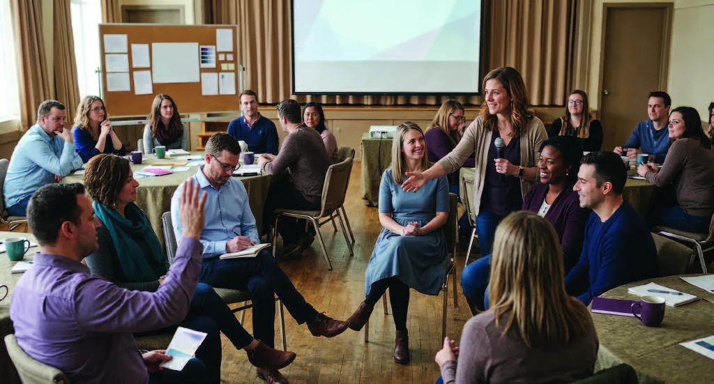 A facilitator leading a large workshop, with participants seated in a circle and at round tables