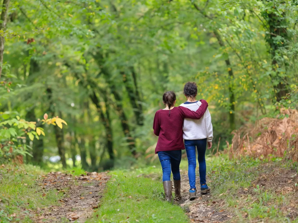 Two people walking arm in arm along a wooded trail